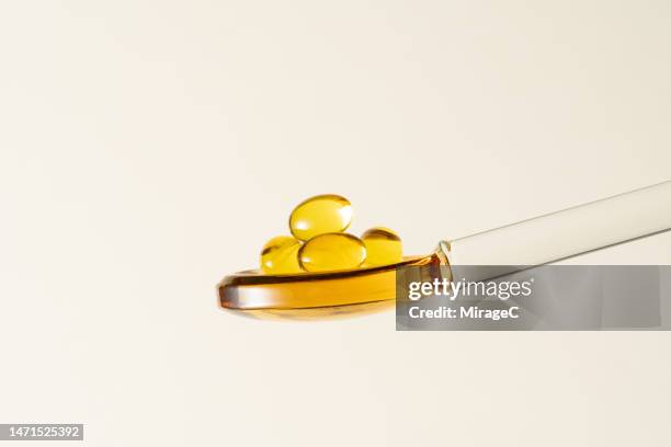 yellow colored soft gel capsules in a glass spoon - cream colored background stock pictures, royalty-free photos & images