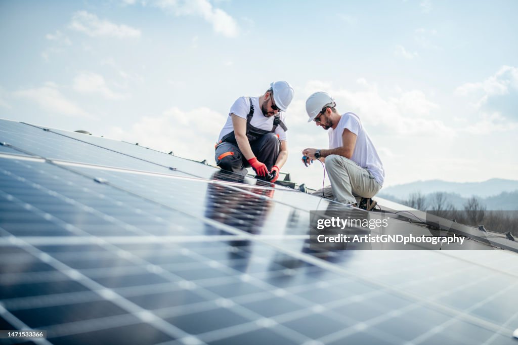 Team von zwei Arbeitern auf dem Dach eines Hauses, die Sonnenkollektoren installieren.