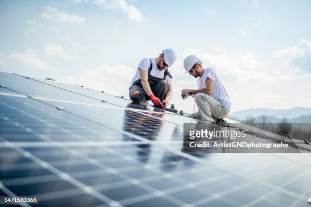 squadra di due operai sul tetto di una casa che installa pannelli solari. - costruttore di tetti foto e immagini stock