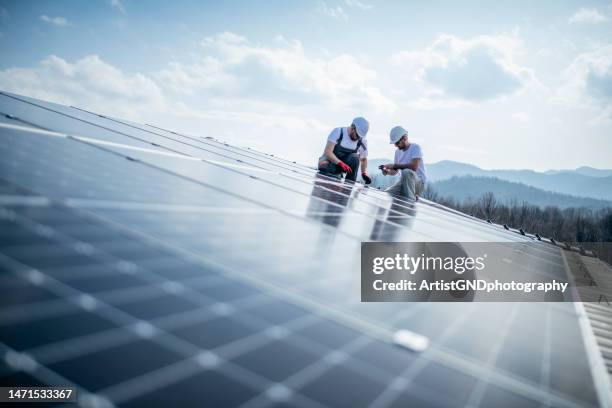 team of two workers on a house's roof installing solar panels. - solsystem bildbanksfoton och bilder