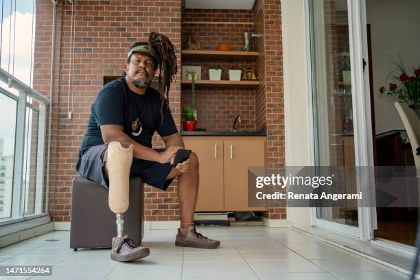 portrait d’un homme avec une prothèse de jambe utilisant un téléphone intelligent à la maison - amputé photos et images de collection
