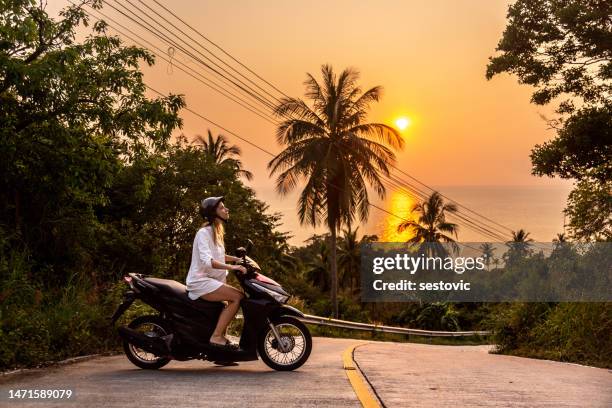 happy smiling woman in a helmet and sunglasses riding motorbike under palm trees on sunset - bali stock pictures, royalty-free photos & images