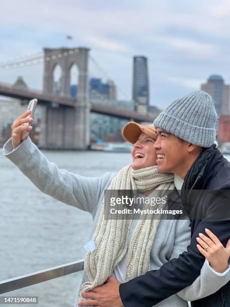 couple taking selfie in nyc with the brooklyn bridge - brooklyn bridge winter stock pictures, royalty-free photos & images