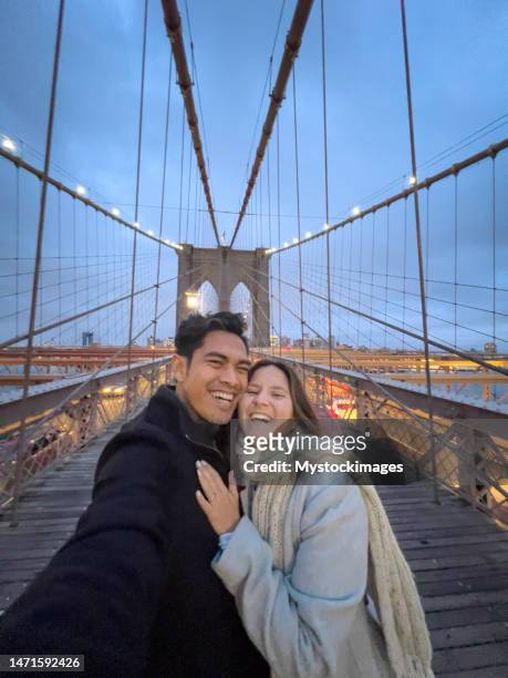 cheerful couple taking selfie on brooklyn bridge at dusk - tourist selfie stock pictures, royalty-free photos & images