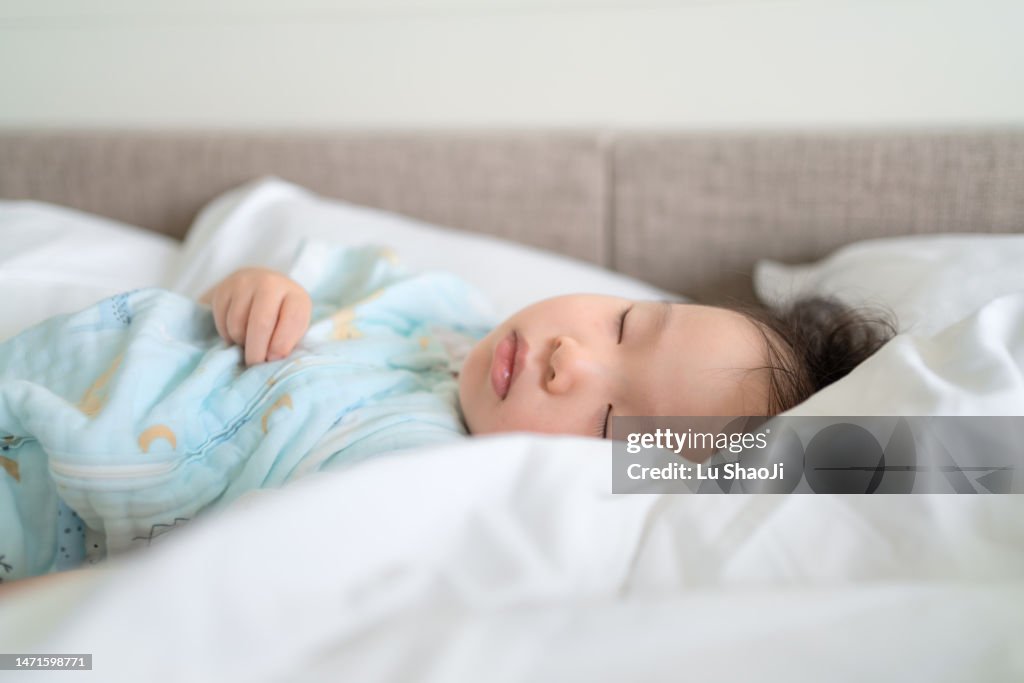 The baby girl sleeps sweetly in the bed.