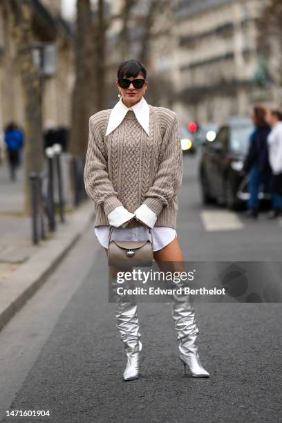 Gili Biegun wears black sunglasses, gold and white pearls pendant earrings, a white shirt with large collar short shirt dress, a brown braided wool...