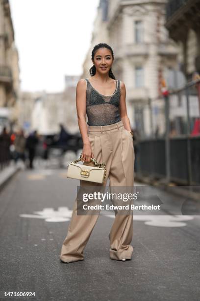 Yuwei Zhangzou wears a black V-neck bra underwear, a beige mesh / fishnet tank-top, high waist beige wide legs suit pants, a beige matte leather with...