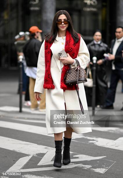 Guest is seen wearing a white coat, red Louis Vuitton scarf, black boots and brown Louis Vuitton bag outside the Palm Angels show during Paris...