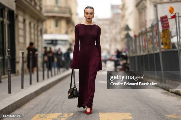 Mary Leest wears gold and diamonds earrings, a burgundy ribbed wool long sleeves / long tube dress, a black shiny leather with red print pattern...