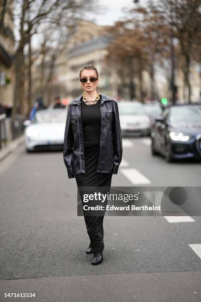 Guest wears black sunglasses, a gold large chain necklace, a black long tube dress, a black shiny leather jacket, black shiny leather block heels...