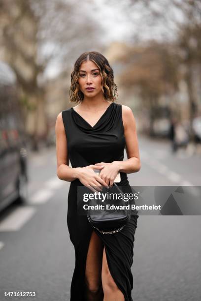 Guest wears a black V-neck / sleeveless long tube slit / split dress, a black shiny leather handbag, outside Atlein, during Paris Fashion Week -...