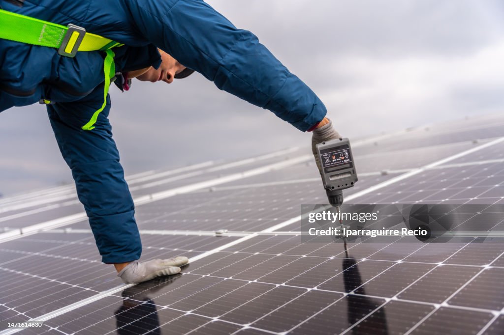Installer technician men mounting photovoltaic solar modules on the roof of the house. Alternative and renewable energy concept. Solar energy, adjusting the panels with a drill