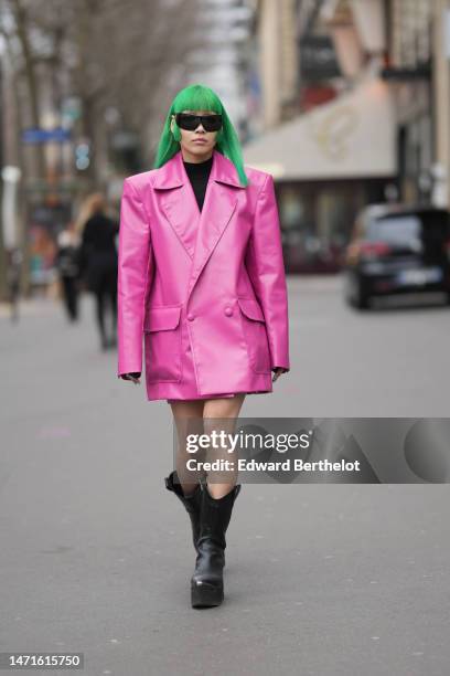 Guest wears black futurist sunglasses, a black turtleneck wool pullover, a neon pink shiny leather oversized blazer jacket, black shiny leather...