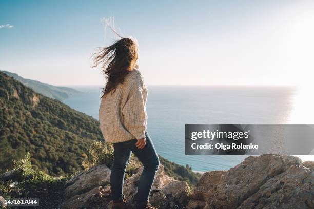 woman looking at the sunset by seaside in mountain area - woman stretching sunset stockfoto's en -beelden