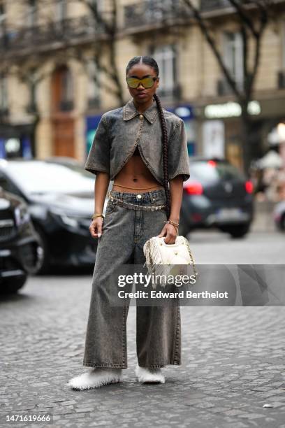 Guest wears black and yellow futurist sunglasses, a gray faded denim short sleeves / asymmetric cropped t-shirt, matching gray denim wide legs pants,...