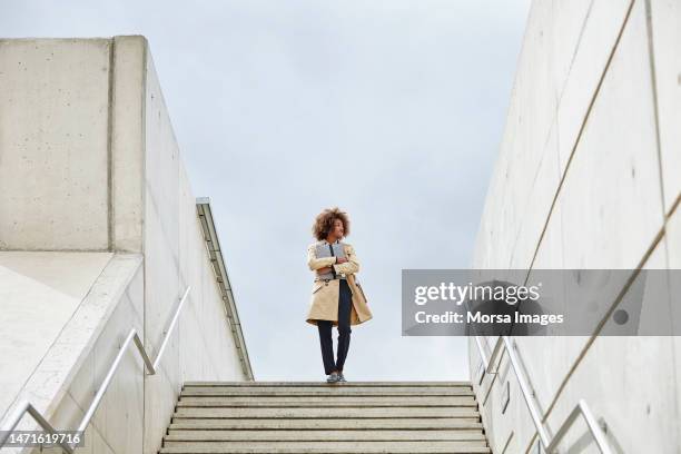thoughtful businesswoman standing on steps - bovenop stockfoto's en -beelden