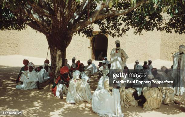 Crowd of men seated in the shade of a tree as they wait to be granted an audience with the Emir of Kano outside the Emir's Palace in Kano, capital...