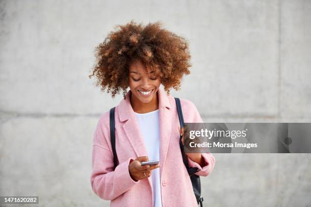 happy woman text messaging through mobile phone - connected city daytime people stock-fotos und bilder