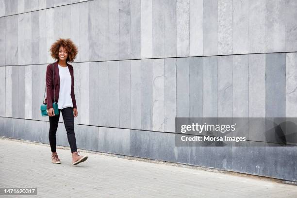 young businesswoman walking on sidewalk by wall - confident woman walking side view stock pictures, royalty-free photos & images
