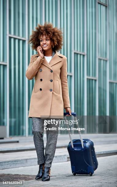 businesswoman with luggage talking on mobile phone - winter coat stock pictures, royalty-free photos & images