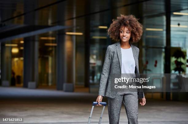 businesswoman with luggage walking outside office - voyage d'affaires photos et images de collection