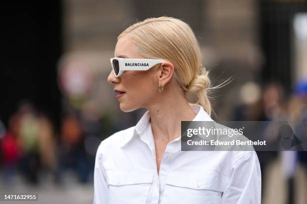 Guest wears beige sunglasses from Balenciaga, gold earrings, a white cropped shirt, outside Balenciaga, during Paris Fashion Week - Womenswear Fall...