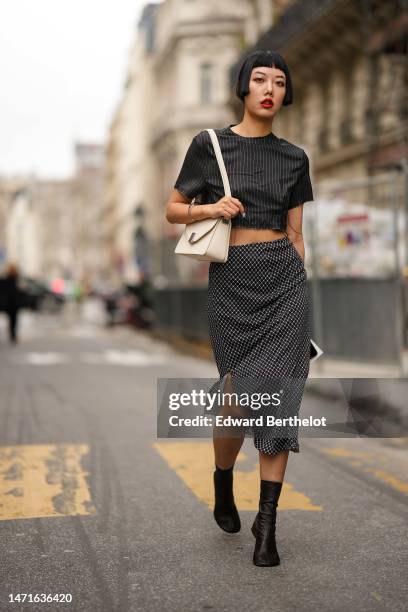 Guest wears a black with white small striped print pattern short sleeves / cropped t-shirt, a white latte matte leather shoulder bag, a silver small...