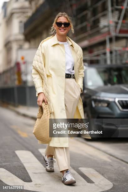Guest wears black sunglasses, gold micro earrings, a white t-shirt, a pale yellow shiny leather buttoned coat, a pale yellow quilted embossed pattern...
