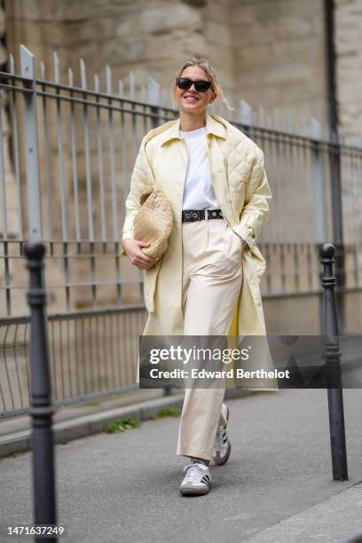 Guest wears black sunglasses, gold micro earrings, a white t-shirt, a pale yellow shiny leather buttoned coat, a pale yellow quilted embossed pattern...