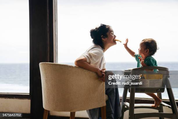 asian woman with her son sitting on the chair eating pizza - two kids looking at each other stockfoto's en -beelden