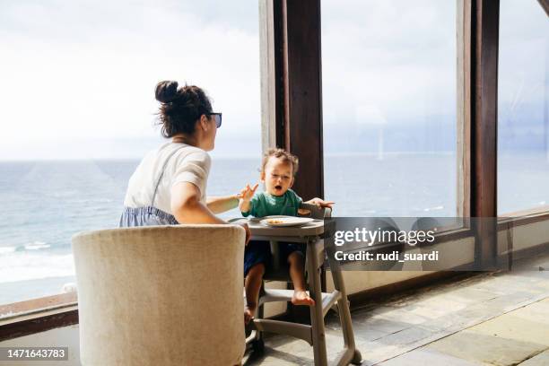 asiatische frau mit ihrem sohn sitzt auf dem stuhl und isst pizza - babystuhl stock-fotos und bilder