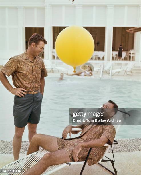 American golfer Ken Venturi with basketball player Bob Cousy, Hawaii, 1962. Cousy is using a straw to drink from a Coca-Cola bottle suspended from a...