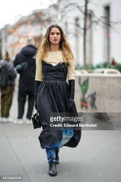 Guest wears neon yellow and diamonds earrings, a beige long sleeves t-shirt, gold chain necklaces, a black V-neck / shoulder-off / long puffy dress,...