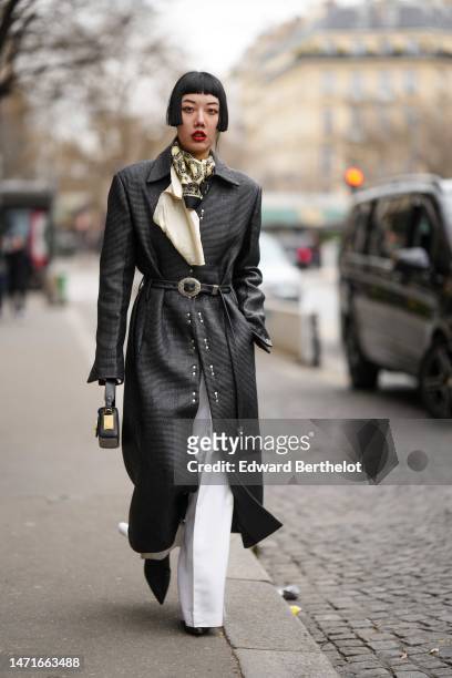 Guest wears a black and pale yellow print pattern silk scarf, a black shiny leather long coat, white denim wide legs pants, a black shiny leather...