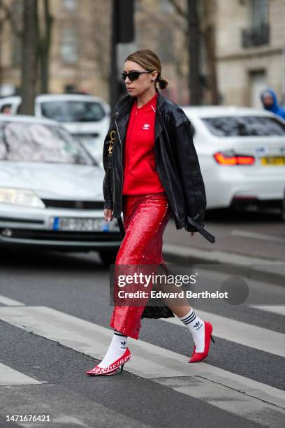 Guest wears black sunglasses, a red zipper sweater from Adidas, a black shiny leather large zipper jacket, a black shiny leather shoulder bag from...