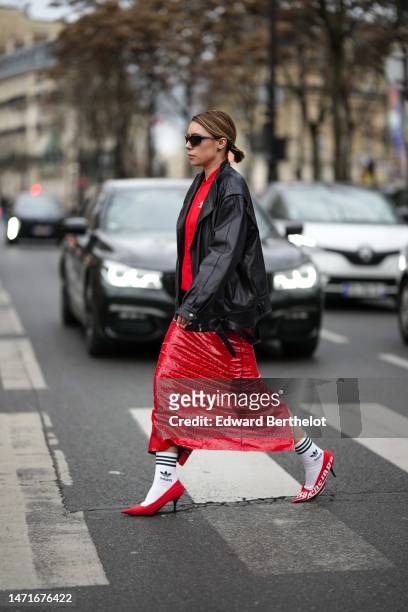 Guest wears black sunglasses, a red zipper sweater from Adidas, a black shiny leather large zipper jacket, a black shiny leather shoulder bag from...