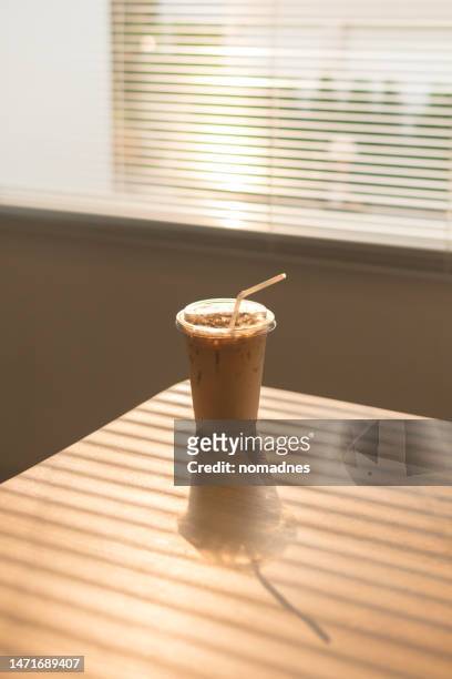 ice latte coffee in disposable cup. cold drink on wood table and sunset behind window background. - breakfast to go stock-fotos und bilder