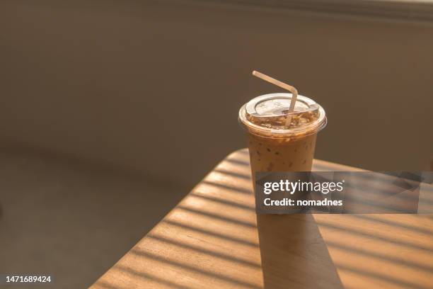 ice latte coffee in disposable cup. cold drink on wood table and sunset behind window background. - cafe latte stock pictures, royalty-free photos & images