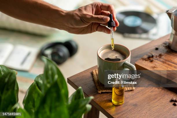 man dropping cbd oil or cannabis oil into a coffee cup while relaxing at home - marijuana herbal cannabis stockfoto's en -beelden