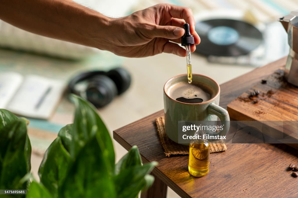 Man dropping CBD oil or Cannabis oil into a coffee cup while relaxing at home