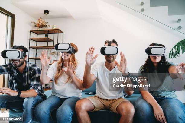 four friends are using virtual reality glasses together on the sofa at home - safety glasses at home stock pictures, royalty-free photos & images