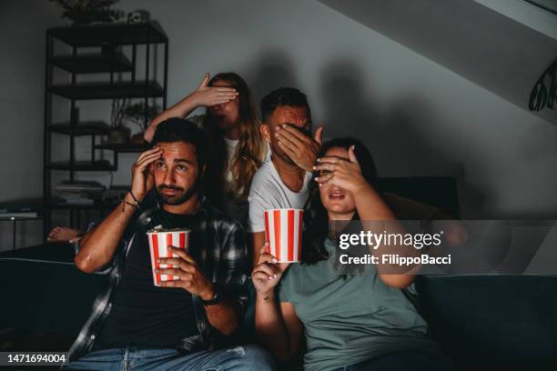 un gruppo di quattro amici sta guardando la tv a casa mentre mangiano popcorn - ambientazione foto e immagini stock
