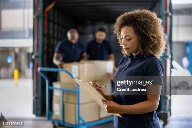 woman supervising the shipping of cargo at a distribution warehouse - freight truck loading stockfoto's en -beelden