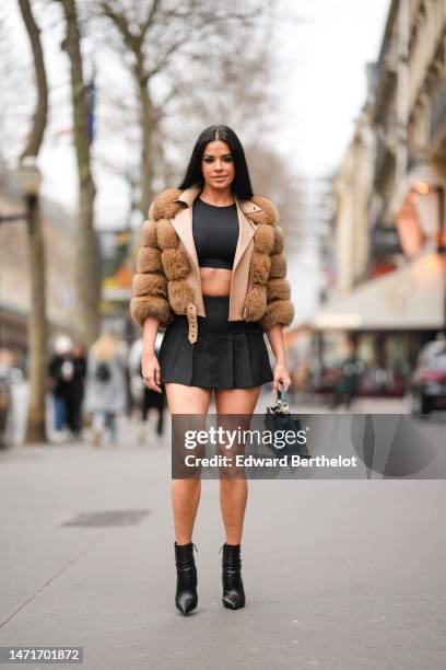 Guest wears a black cropped top, a brown quilted fur jacket, a black pleated / accordion short skirt, a blue gray shiny leather handbag, black shiny...