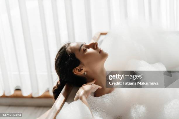 young woman relaxing in bath tub full of foam bubbles. self care and mental health concept. - frau badewanne stock-fotos und bilder