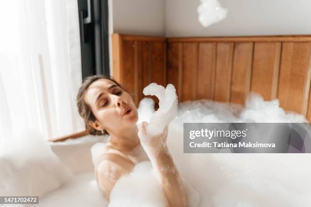 young woman relaxing in bath tub full of foam bubbles. self care and mental health concept. - woman bath bubbles stock-fotos und bilder