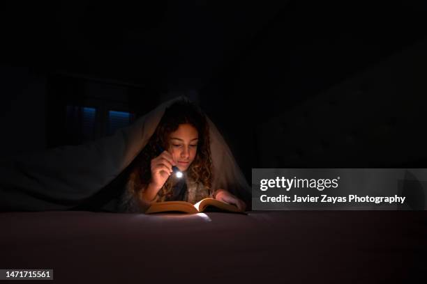 girl reading a book in bed with a flashlight under the quilt - conto-de-fadas imagens e fotografias de stock