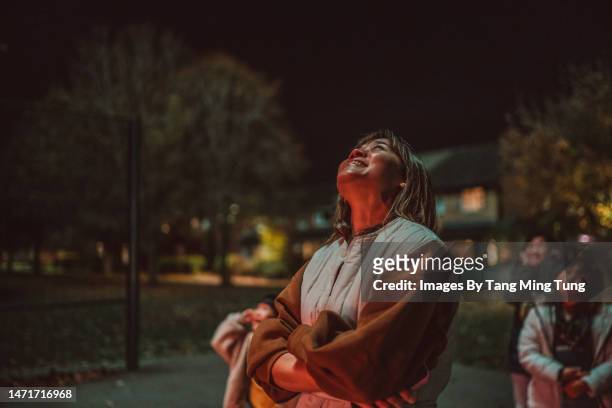 young asian woman admiring firework with her family in public park - family fireworks stockfoto's en -beelden