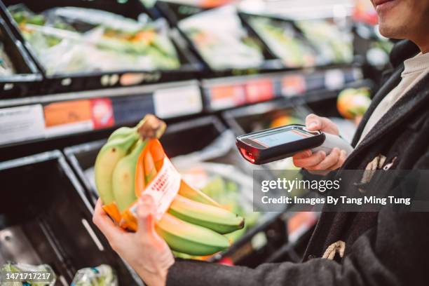 close-up of a young man using handheld barcode reader scanning a bunch of bananas while shopping in supermarket - scan barcode stock pictures, royalty-free photos & images