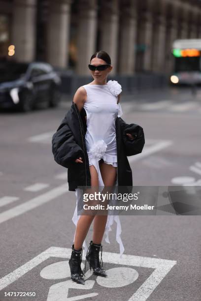 Fashion week guest seen wearing black shades by Balenciaga, a black bomber jacket, a white dress and black Balenciaga le Cagole heels before the...